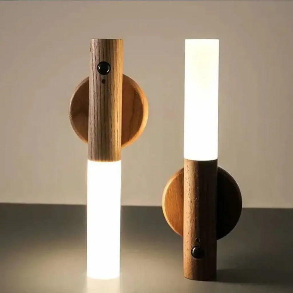 Two modern minimalist wall sconces with cylindrical wooden bodies, circular backplates, and glowing white LED light bars, shown against a neutral beige background.
