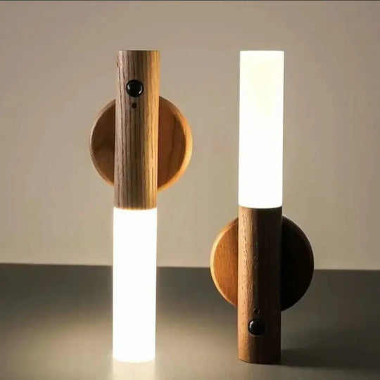 Two modern minimalist wall sconces with cylindrical wooden bodies, circular backplates, and glowing white LED light bars, shown against a neutral beige background.